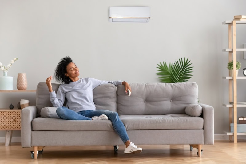 Female homeowner enjoying the cool breeze on her couch thanks to a ductless mini split mounted to wall.